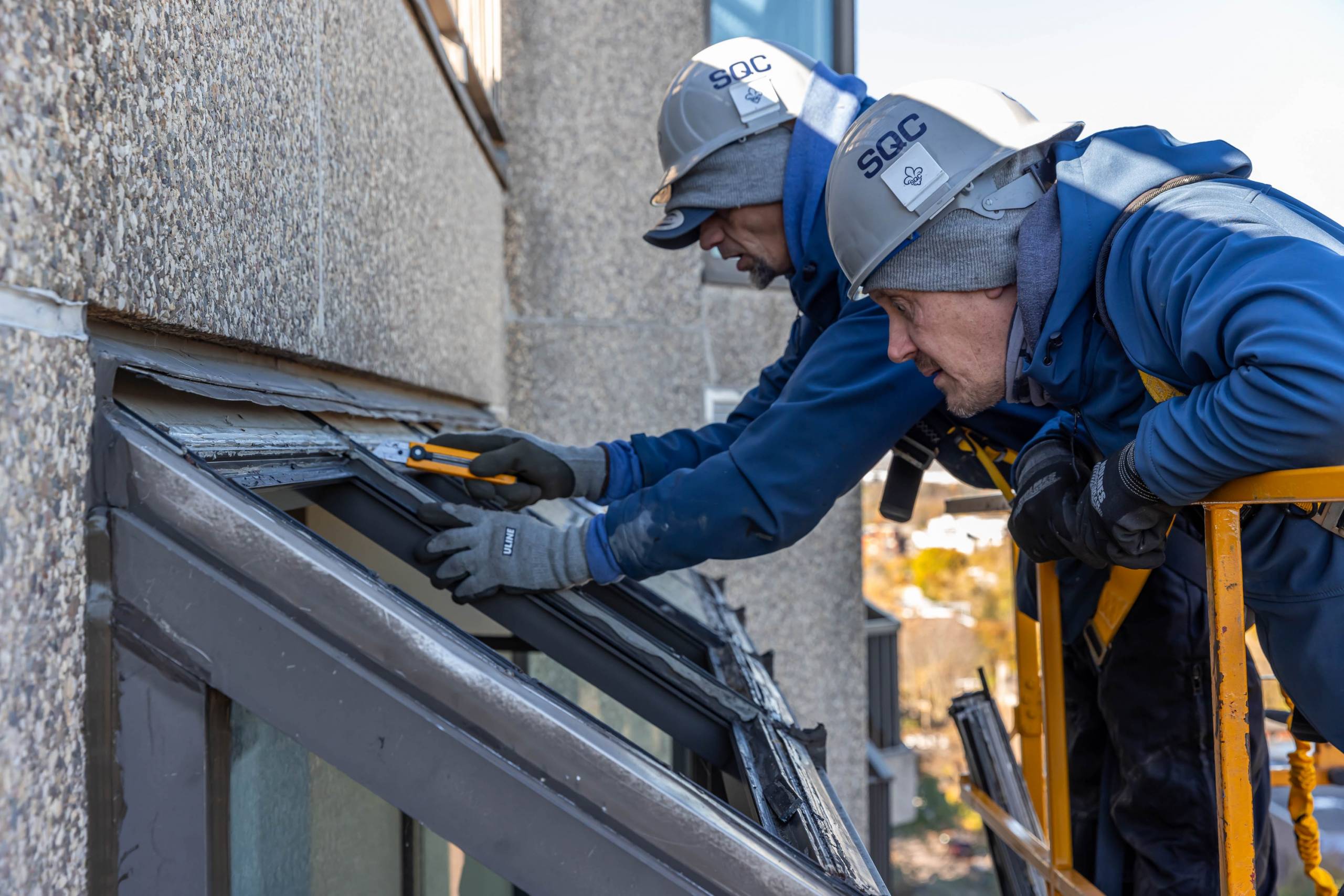 Employés de Basco Portes et Fenêtres avec casques du Syndicat québécois de la construction effectuant des manoeuvres complexes de réparation de fenêtres de solarium